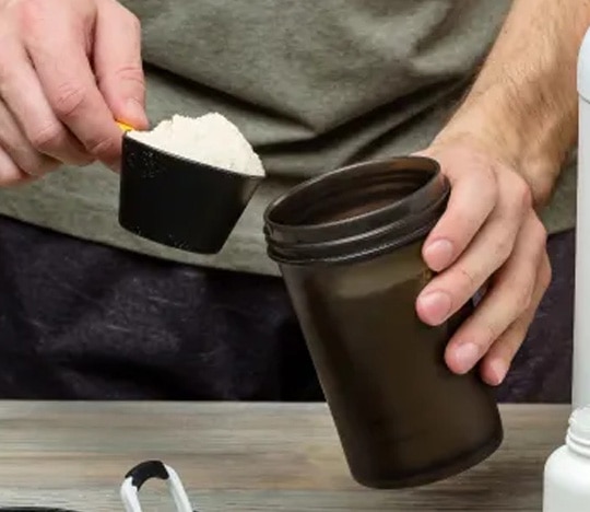 man pouring pre-workout powder into a cup.